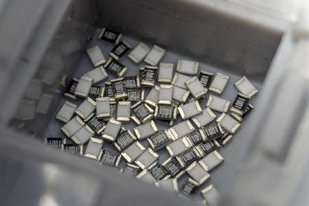 Abstract close-up of grey scattered microscopic 0603 SMT surface mount chip resistors power electronics components sorted in grey container background in random patternの写真素材
