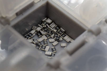 Abstract close-up of grey scattered microscopic 0603 SMT surface mount chip resistors power electronics components sorted in grey container background in random patternの写真素材