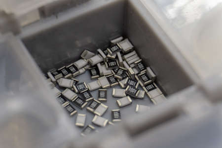 Abstract close-up of grey scattered microscopic 0603 SMT surface mount chip resistors power electronics components sorted in grey container background in random patternの写真素材