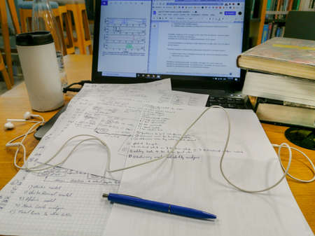 Realistic library environment electronics engineering scientific paper writing for conference with laptop, books, coffee, earphones and water bottle. Close up of pen.の写真素材