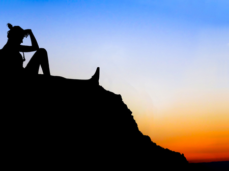 Silhouette of girl in depression sitting at sunsetの写真素材