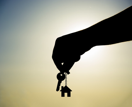 Holding house keys on house shaped keychainの写真素材