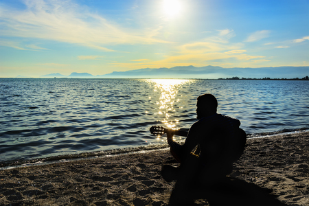 Silhouette.Young men playing guitar while sitting on the beach.の写真素材