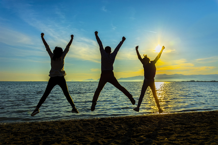Silhouette group of friends having fun jumps on the beach sunset.の写真素材