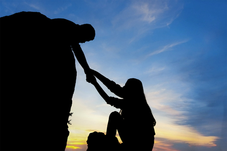 Teamwork couple helping hand trust assistance silhouette in mountains, sunset.の写真素材