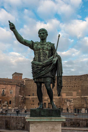 Bronze statue of the Roman Emperor Augustus on Via dei Fori Imperiali in front of old brick...