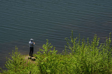 Fisherman man fishing with spinning rod on lake shoreの写真素材