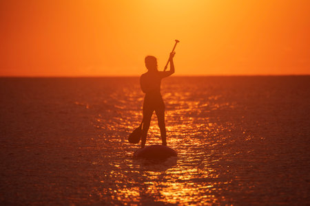 Silhouette of a woman on a stand up paddle board at sunset. SUP. Stand up shovel. Silhouette of woman paddleboarding at sunset. Canakkale, TÃ¼rkiye.の写真素材