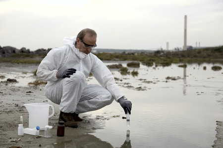 Worker in a protective suit examining pollution in the water at the industry.の写真素材