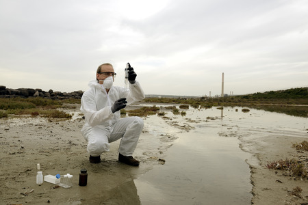 Worker in a protective suit examining pollution in the water at the industry.