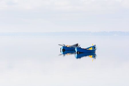A pair of blue boats remain anchored in the middle of the lagoon. dawn twilight. In the background the island of Sant'Antioco, Sardinia Southwest. Lagoon Bruncu Teula.の写真素材