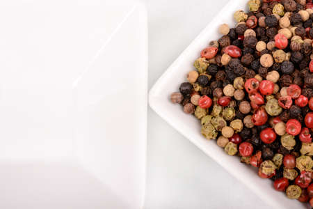 Colorful peppercorns in a white mixing bowl. Horizontal cut with white background.