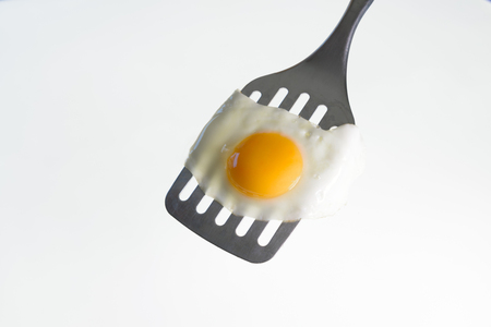 Fried egg on the steel spatula, ready to be served. White background.の写真素材