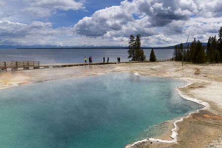 Yellowstone, United States - May 31, 2015: Clear, aqua hot spring with deep central hole, steam and limy shoreline, people on boardwalk, West Thumb area of Yellowstone National Park, Wyoming.のeditorial素材