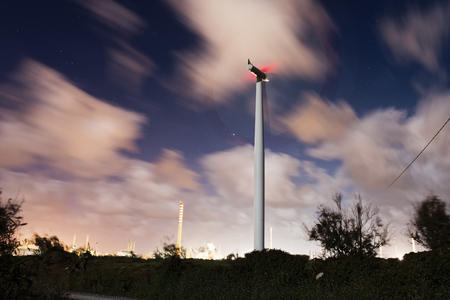 Windmill in the night with industries and cloudy sk.