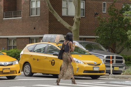New York City, USA - June 08, 2017: New York yellow taxi cab stop at pedestrians traffic lights crossing the street in pedestrian crossing. American woman crosses the zebra crossing while the taxis are stationary.のeditorial素材