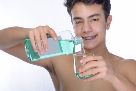 Cute teenager with white background, wearing braces on his teeth. Spray a disinfectant mouthwash in the throat. Portrait second floor blurred.の写真素材
