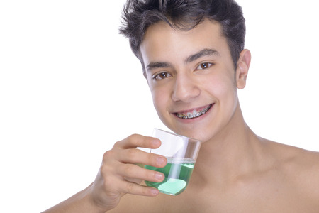 Cute teenager with white background, wearing braces on his teeth. Use mouthwash for oral hygiene.の写真素材