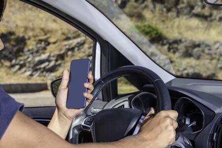Young driver, using smartphone, on the road in the car. Distraction and danger on the road.