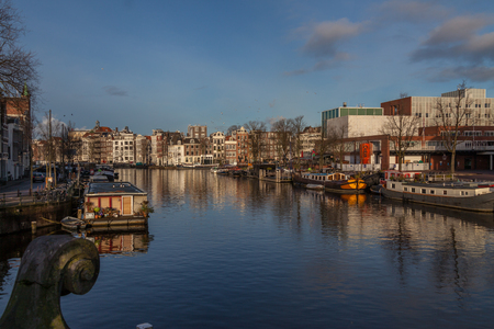 a bridge on water canal in Amsterdam on a sunny winter autumn day with traditional architecture reflecting in waterのeditorial素材