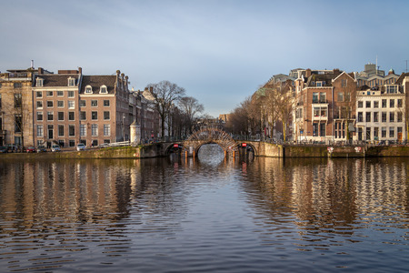 a bridge on water canal in Amsterdam on a sunny winter autumn day with treesの写真素材