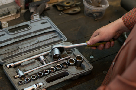 Mechanic take tool from the set tools, wich lying on the desktop in garage