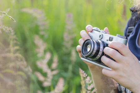 Hands of a girl holding a vintage camera on a background of high grassの写真素材