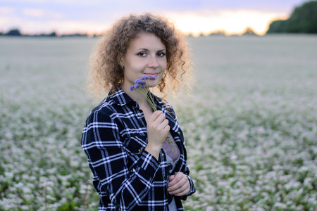 The girl sniffs a bouquet of cornflowers against the background of the evening sky and a flower fieldの写真素材