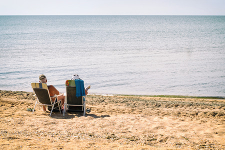 Senior couple sitting on the beach by the seaの写真素材