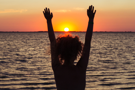 The girl raising her hands to the sunset at sea, enjoying nature and freedomの写真素材