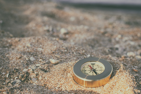A compass showing the direction lies on sand with seashellsの写真素材