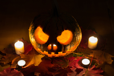 Scary halloween pumpkin with leaves and burning candlesの写真素材