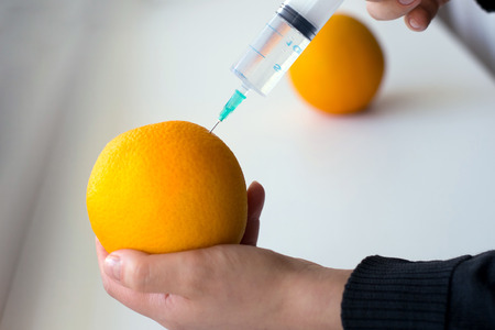 Photo of hand making injection into an orange on a light backgroundの写真素材