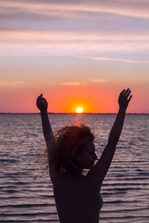 The girl raising her hands to the sunset at sea, enjoying nature and freedomの写真素材