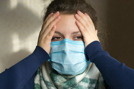 A girl with a medical mask on her face holds on to her headの写真素材
