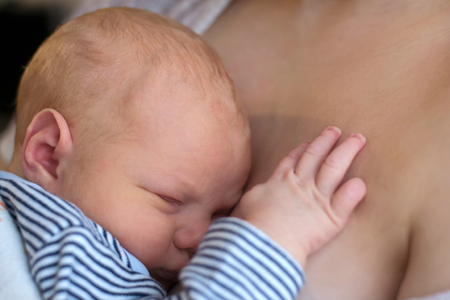 Cute newborn baby sleeping on his mother's breastの写真素材