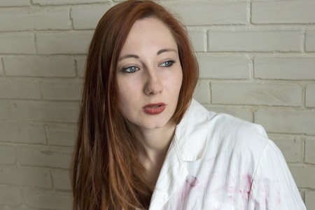 Portrait of a red-haired girl in a white shirt against a brick wall backgroundの写真素材