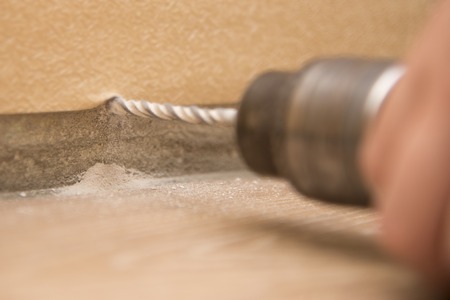 The hand holds the drill near the wall, close-up, the theme of repair work and buildingの写真素材