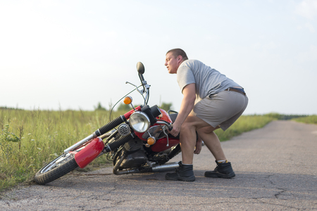 A man lifts a heavy motorcycle that fell after an accidentの写真素材