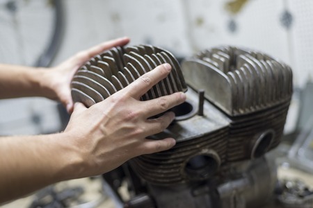A man fixing a motorcycle motor in a garage,hands holding a cylinder, close-upの写真素材