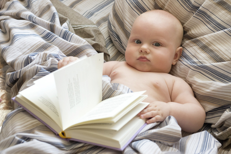 Little cute baby is lying in bed with a book