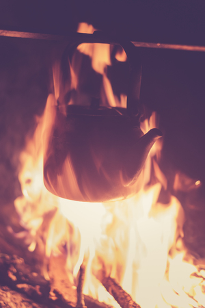 The kettle is heated on a bright fire at night outdoor, toned photoの写真素材