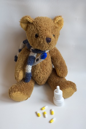 Cute teddy bear in a scarf with a thermometer and medicine on a light backgroundの写真素材