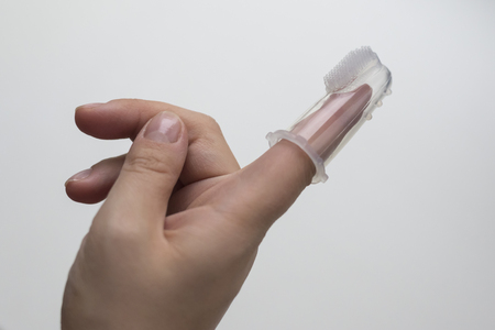 Silicone brush for cleaning the teeth of babies, put on mother's finger, on a light backgroundの写真素材