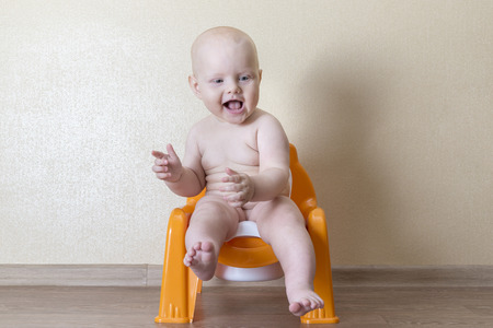 Naked baby sitting on an orange pot for boysの写真素材