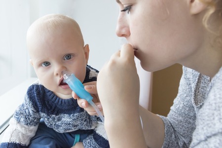 Mom cleans baby's nose from mucus using a nasal aspiratorの写真素材