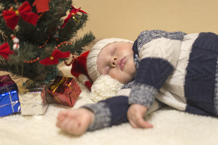 Little baby in Santa's hat sleeping under the Christmas tree with giftsの写真素材
