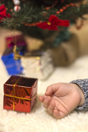 The hand of the little child lies behind the gift of the Christmas treeの写真素材