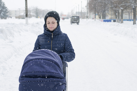 A young mother walks with a stroller on a snowy winter dayの写真素材