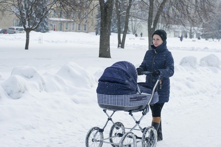 A young mother walks with a stroller on a snowy winter dayの写真素材
